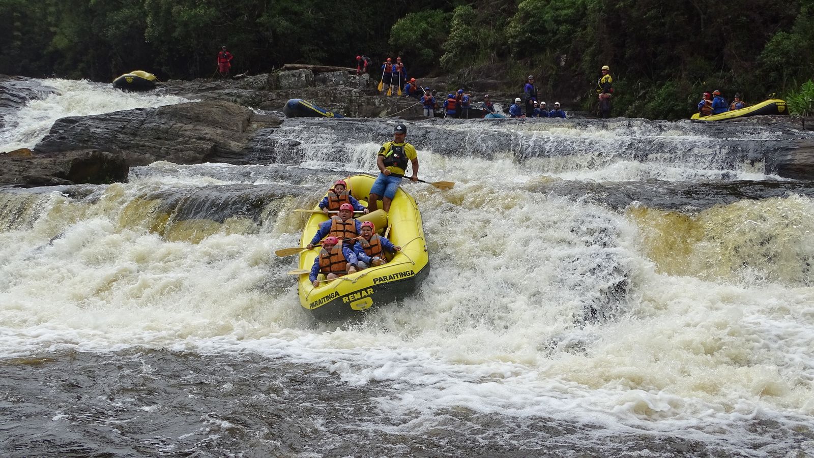 Bote descendo uma queda d'água larga no Santa Virgínia, com a turma da Montana assistindo das pedras
