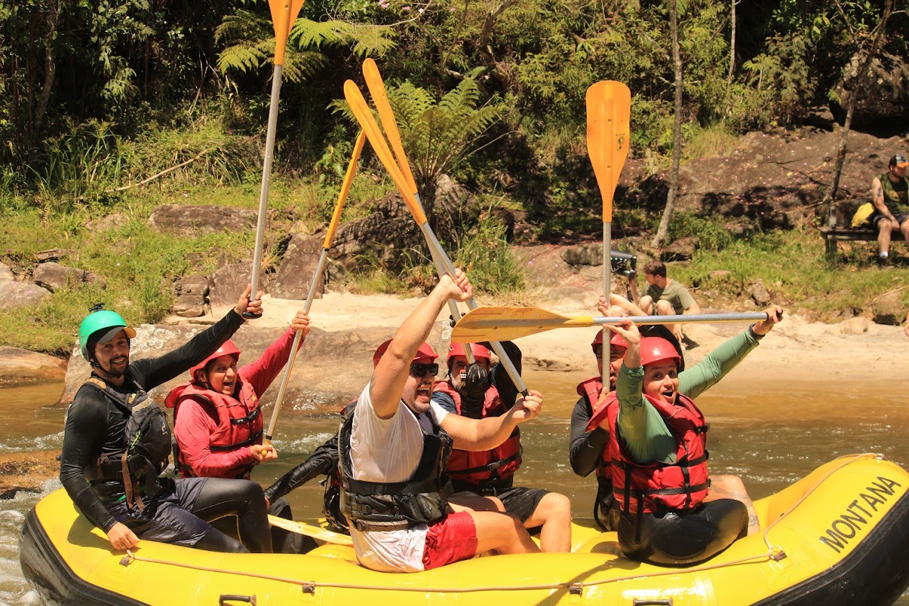 Turma comemorando com os remos pro alto no bote, na beira da mata