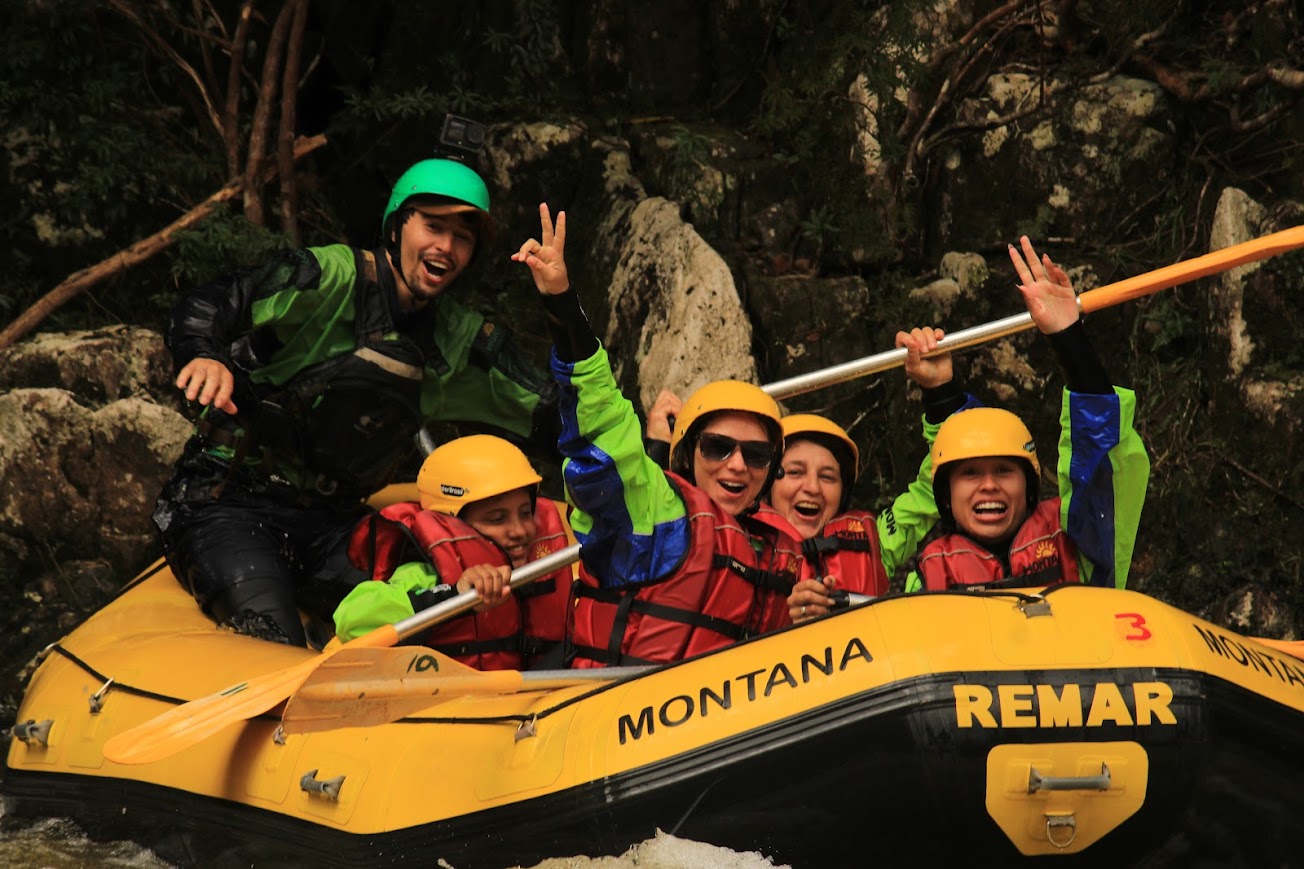 Grupo comemorando no bote em frente a paredão de pedra e mata fechada